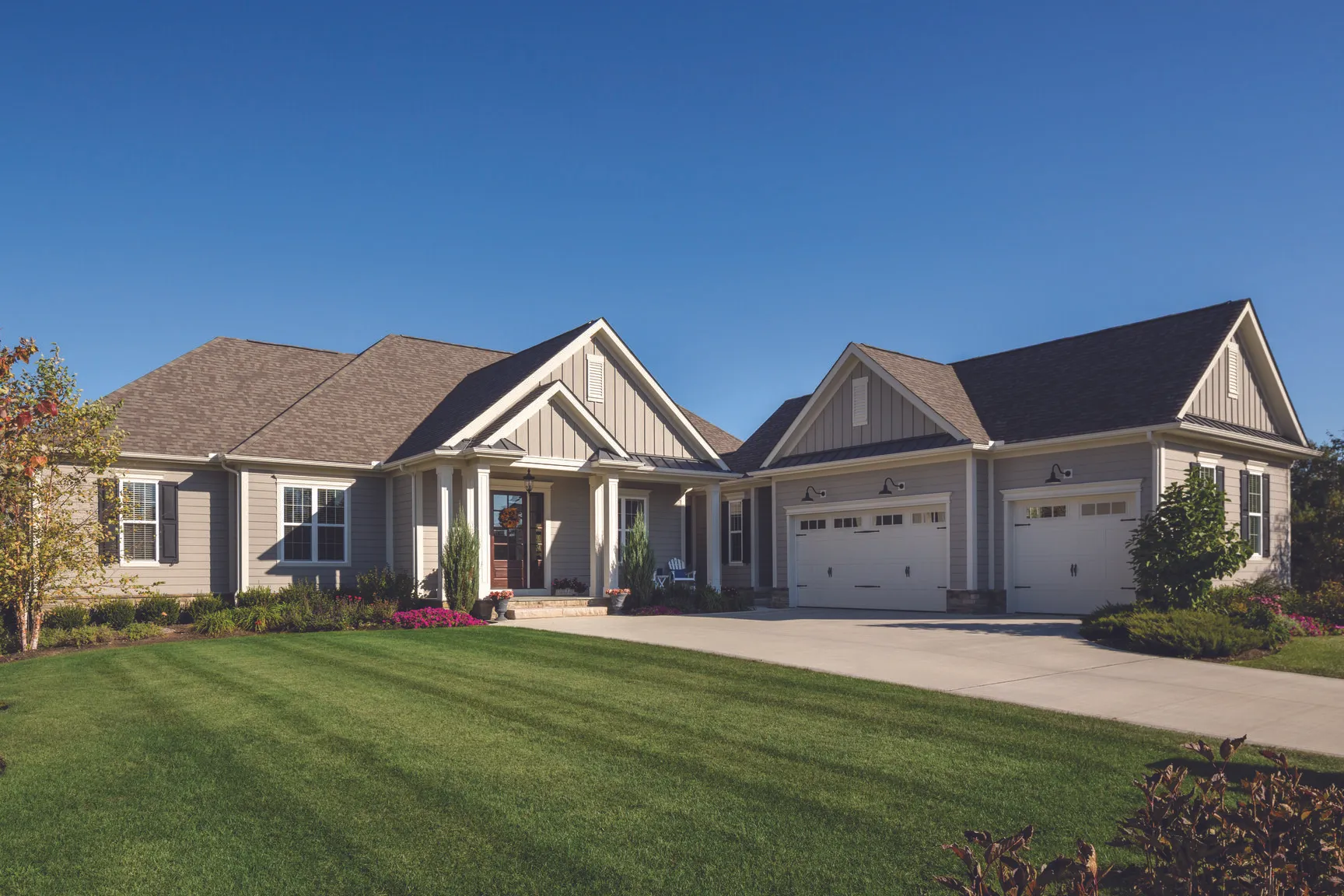 Single-story house with gray siding, white trim, three-car garage, and neatly manicured front lawn under a clear blue sky.